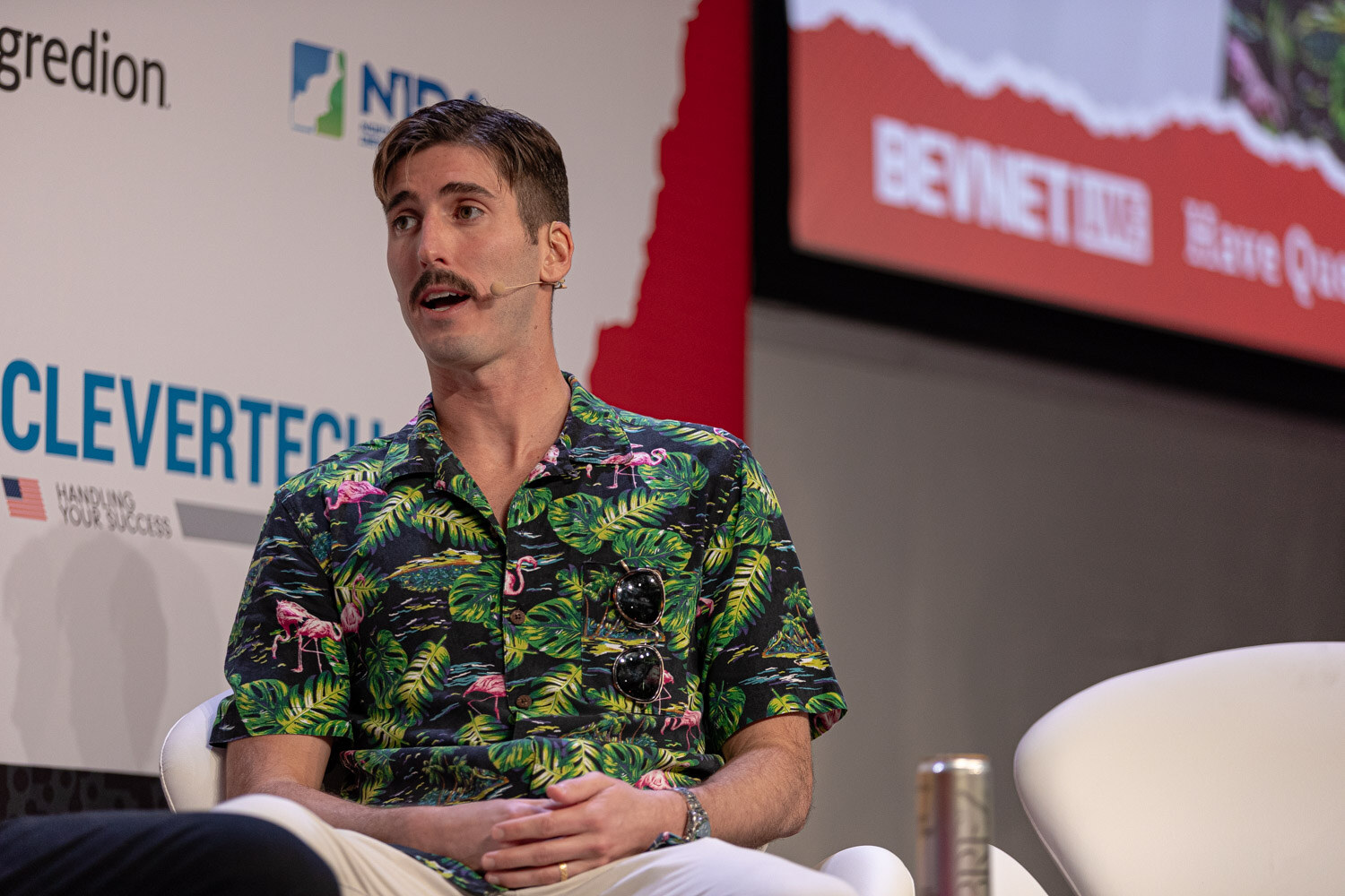 Panelist in a flamingo-print shirt sits relaxed with hands folded.