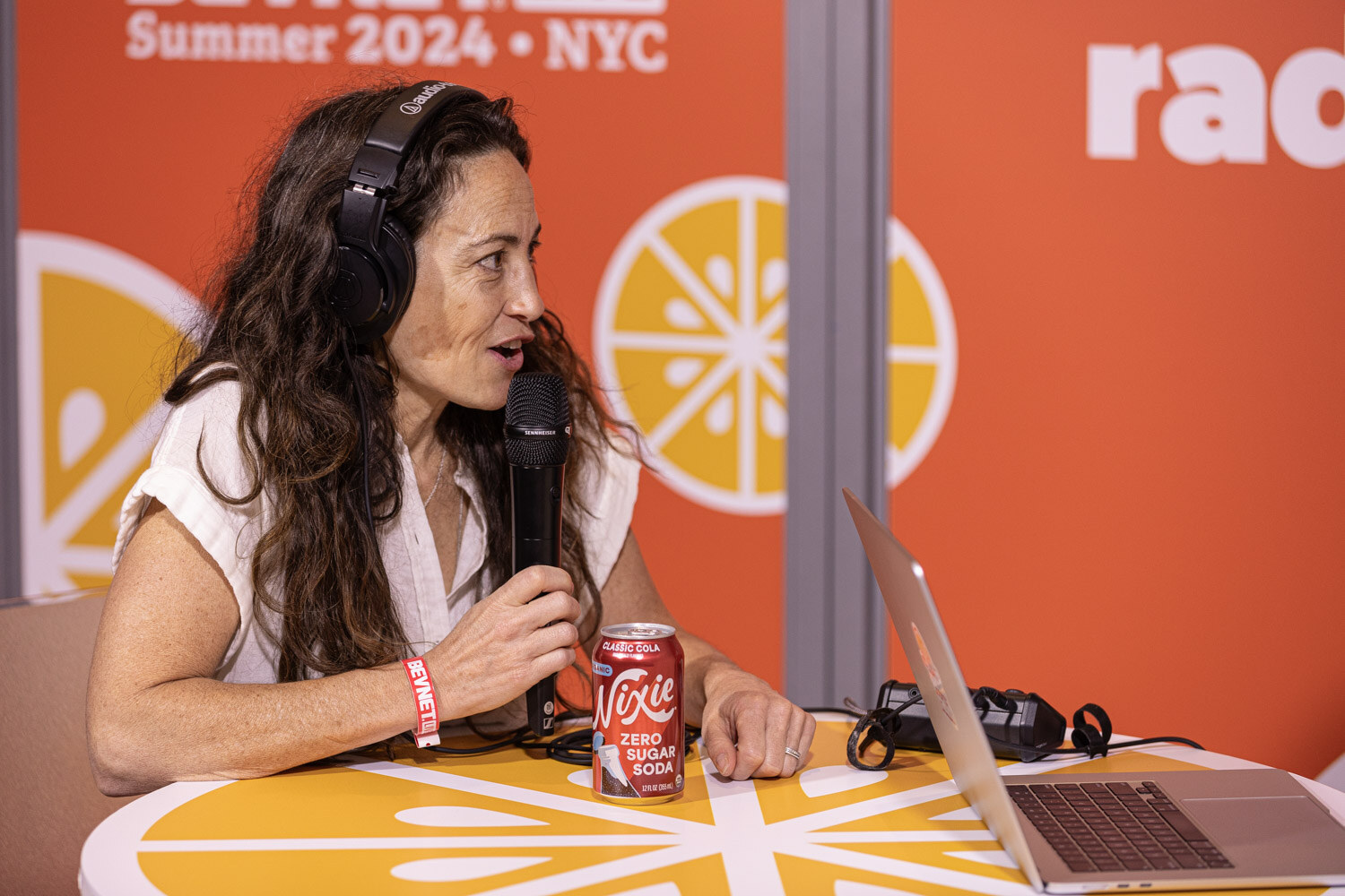 Guest in a cream top speaks into a microphone at the Taste Radio livestream table.