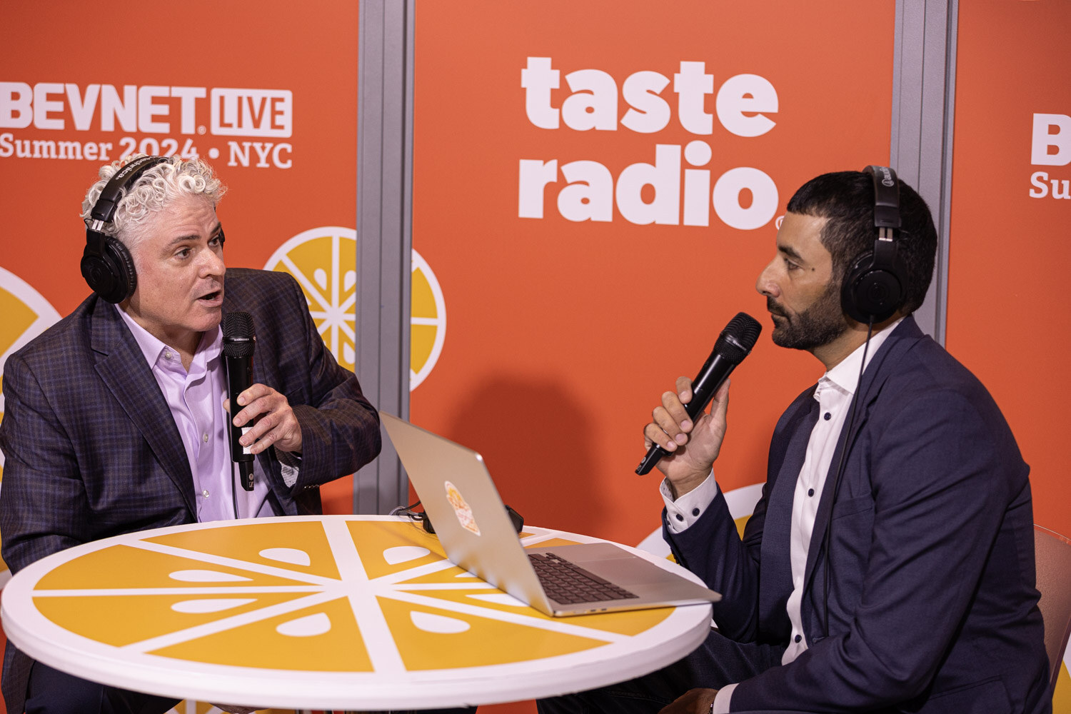 Host interviews a guest in headphones across the orange Taste Radio table.