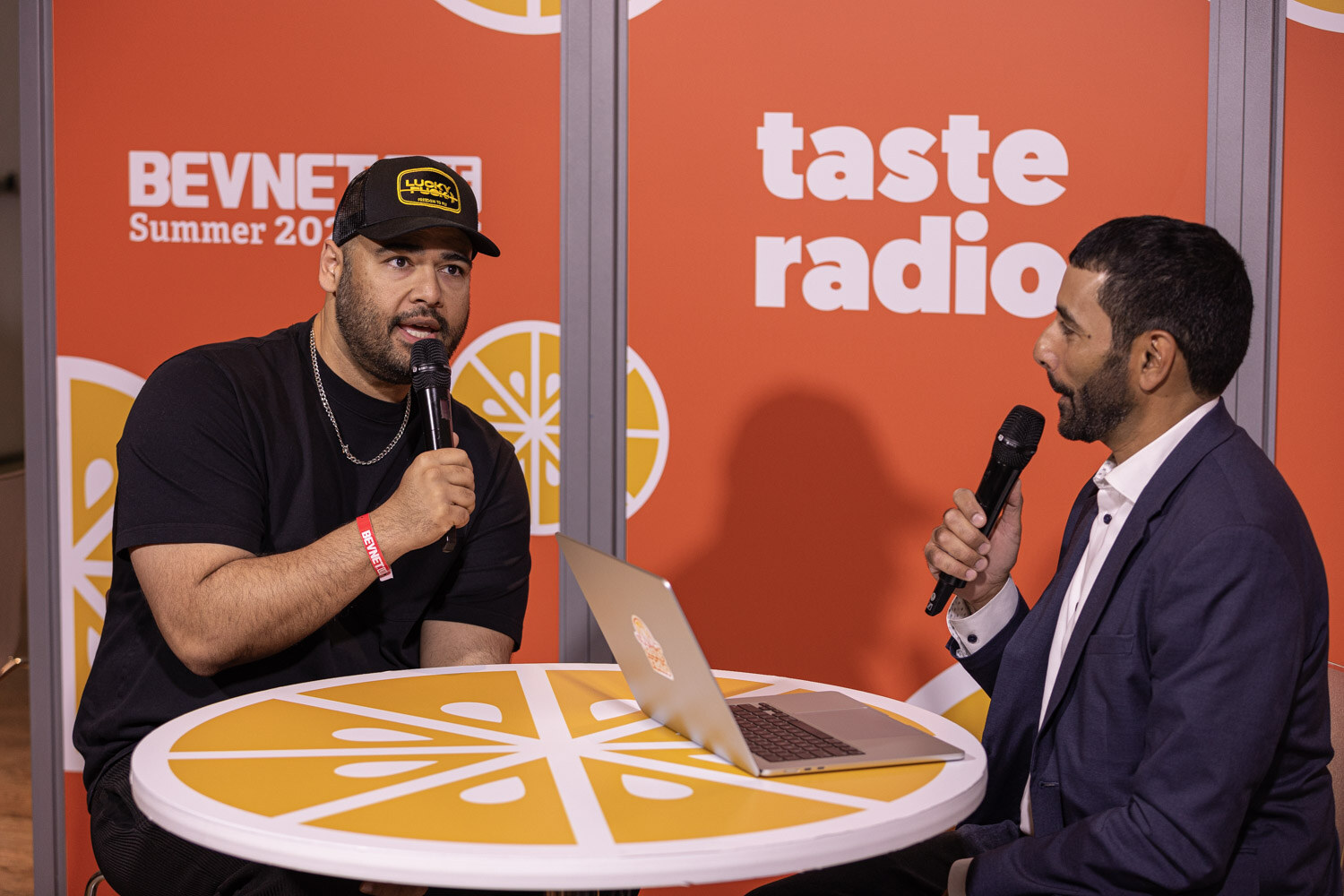 Host and guest in a black cap talk across the table at the Taste Radio set.
