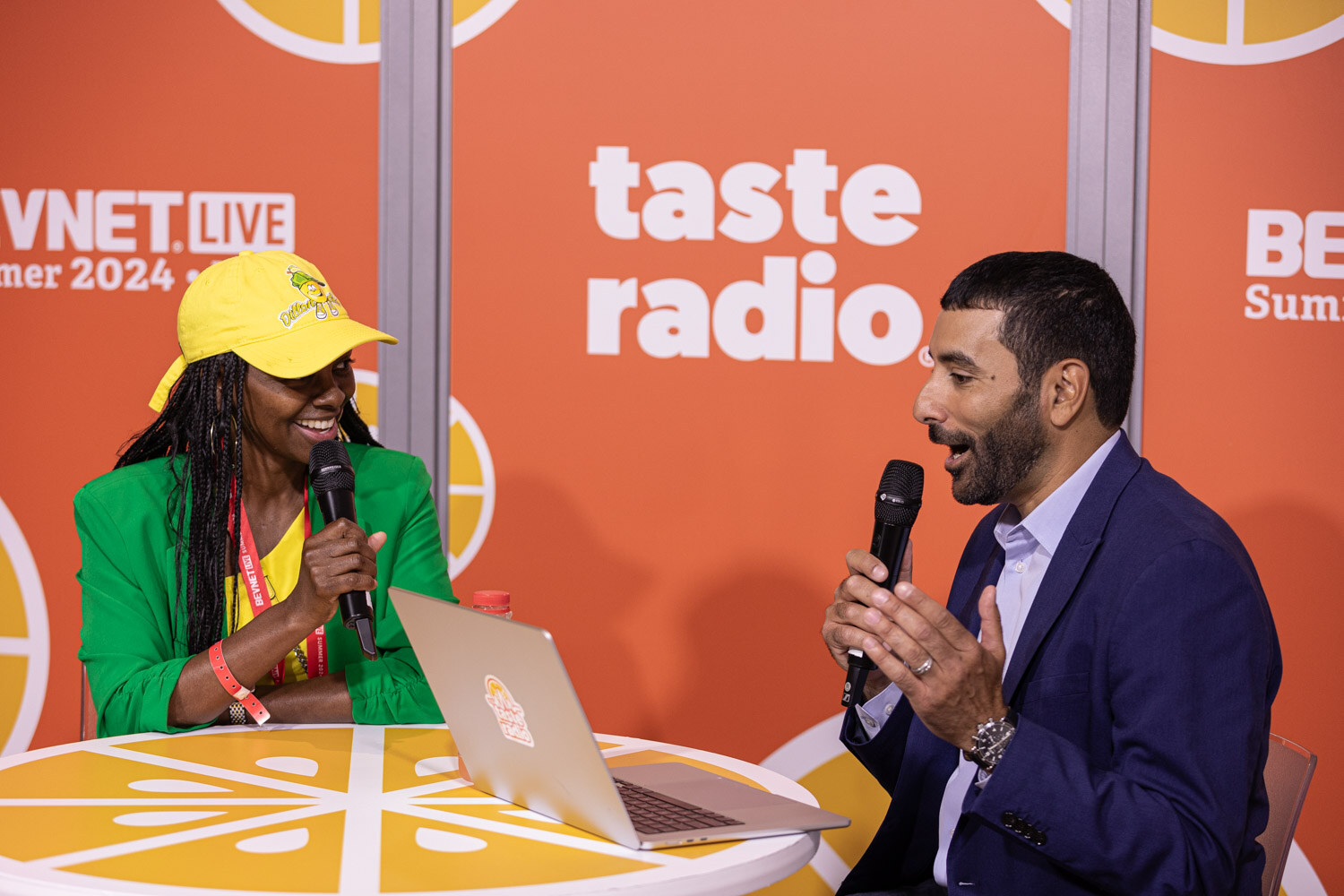 Host in a navy suit and guest in a green blazer talk at the Taste Radio table.