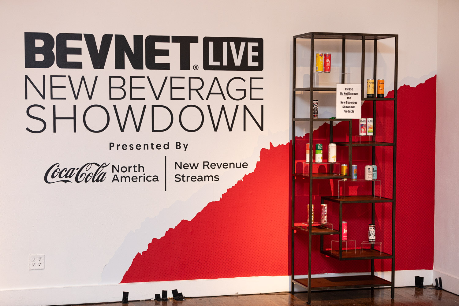 BevNET Live New Beverage Showdown sign with a shelf of product cans.
