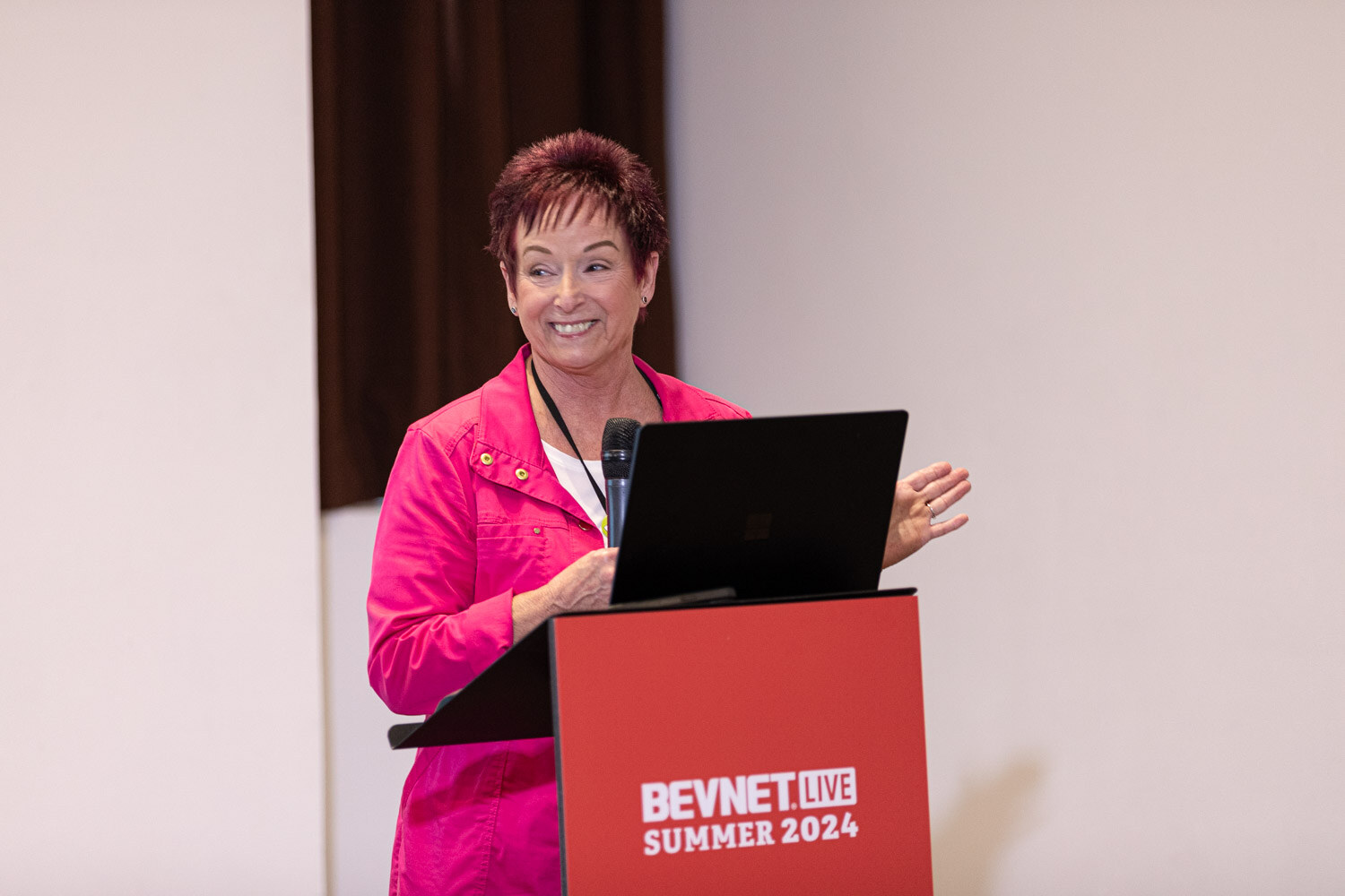 Presenter in a bright pink jacket smiles at the podium during the Craft the Perfect Collagen workshop.