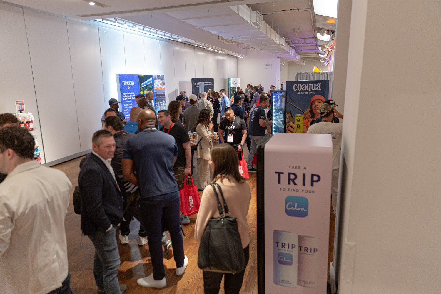 Attendees in a hallway lined with exhibitor booths, with a tall Calm Trip display in the foreground.