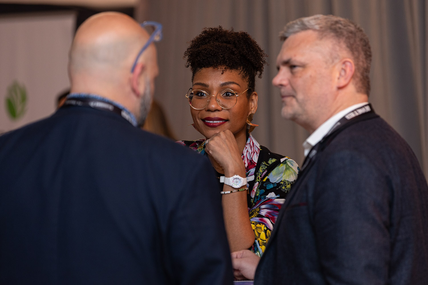 A woman in a floral top looks at the camera between two men with lanyards.