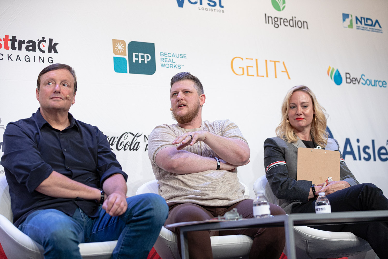 Three people seated in white chairs in front of a Gelita and BevSource backdrop, one with a clipboard.