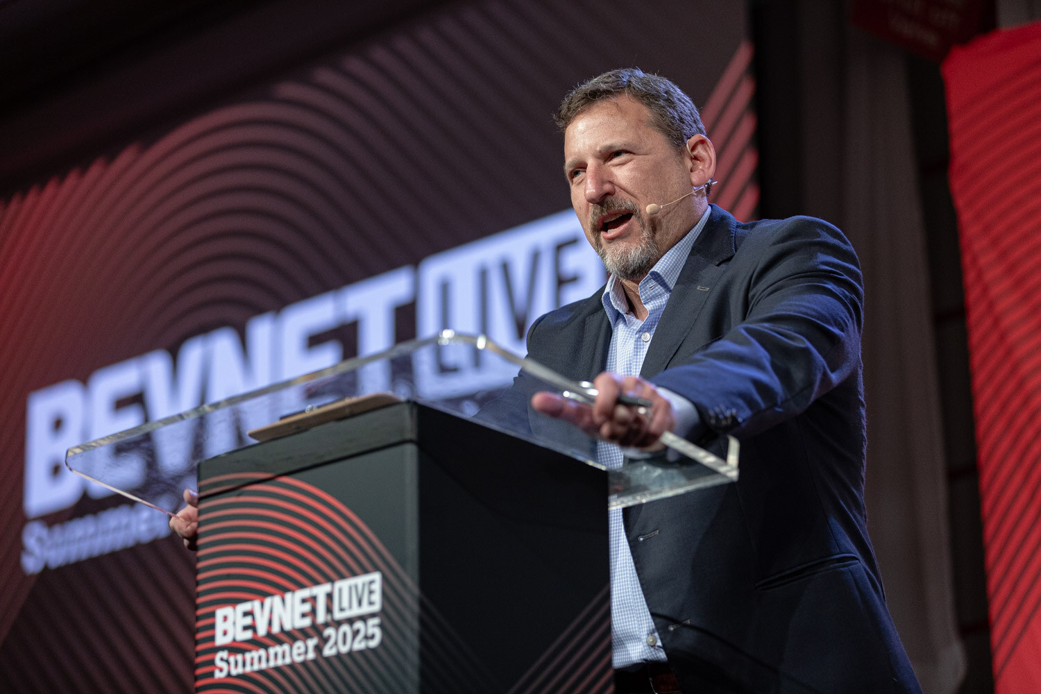 A man in a navy blazer gestures with one arm over a podium marked BevNET Live Summer 2025.