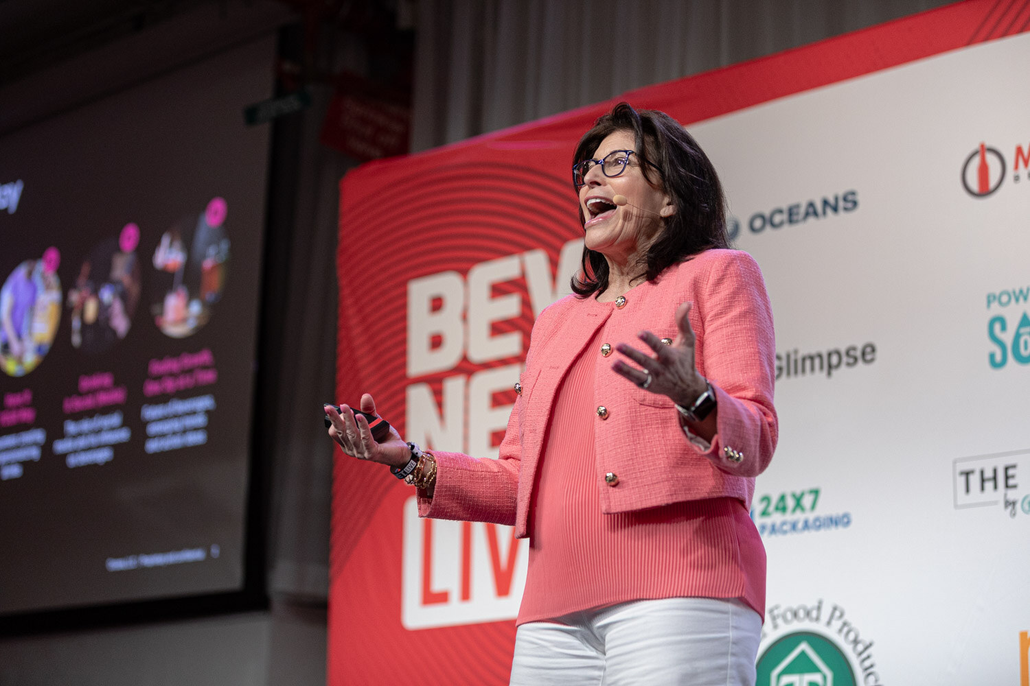 A woman in a coral tweed jacket and glasses speaks and gestures on stage in front of the BevNET Live banner.