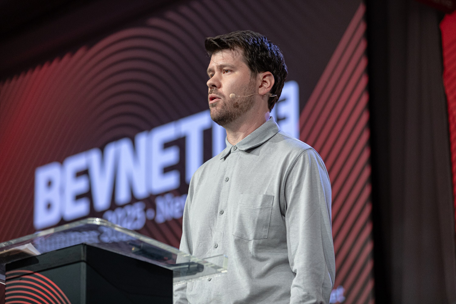 A man in a gray shirt speaks at a podium in front of a large BevNET Live screen.