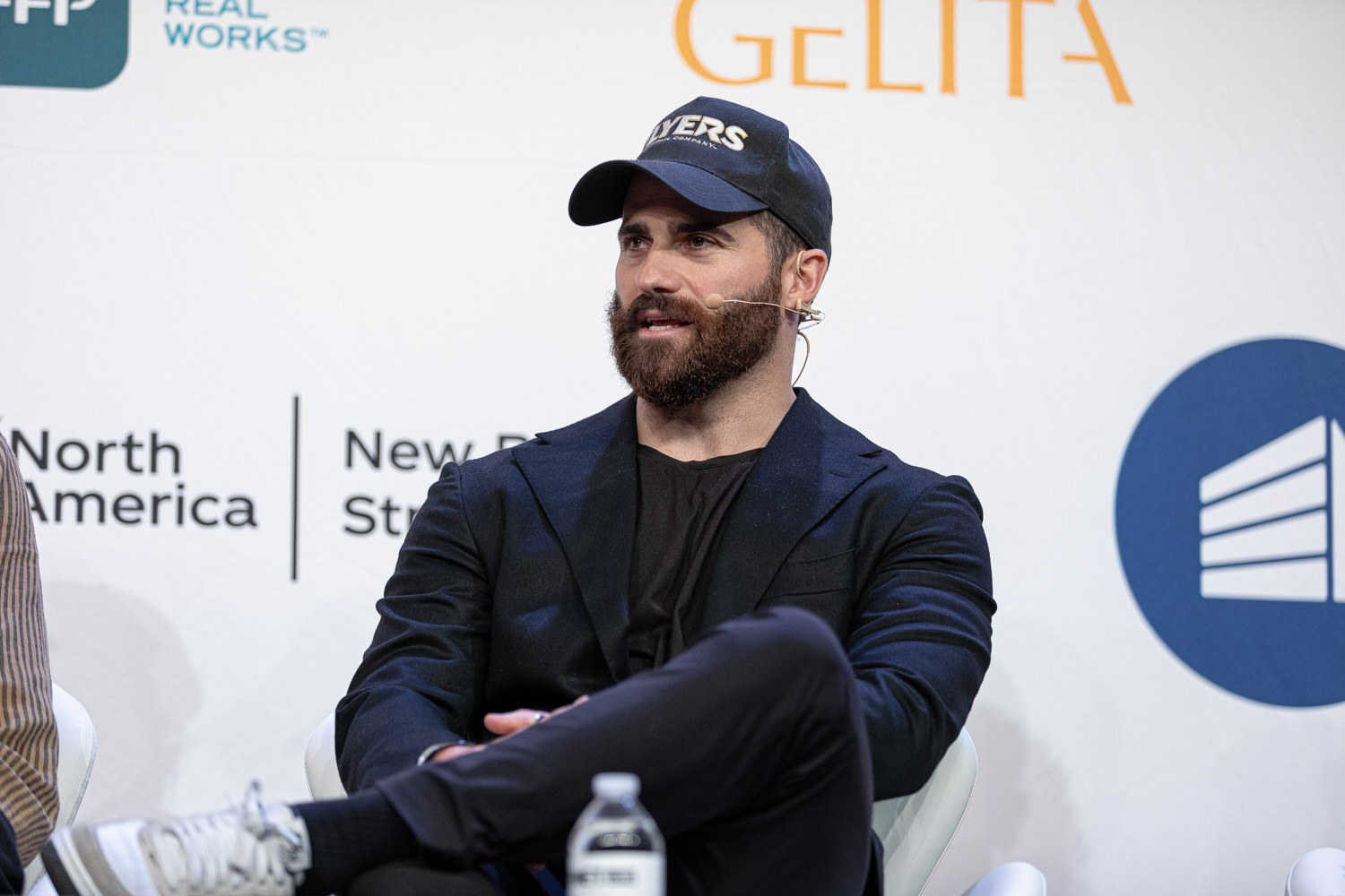 A bearded man in a ball cap and black jacket sits in front of a Coca-Cola North America sign.