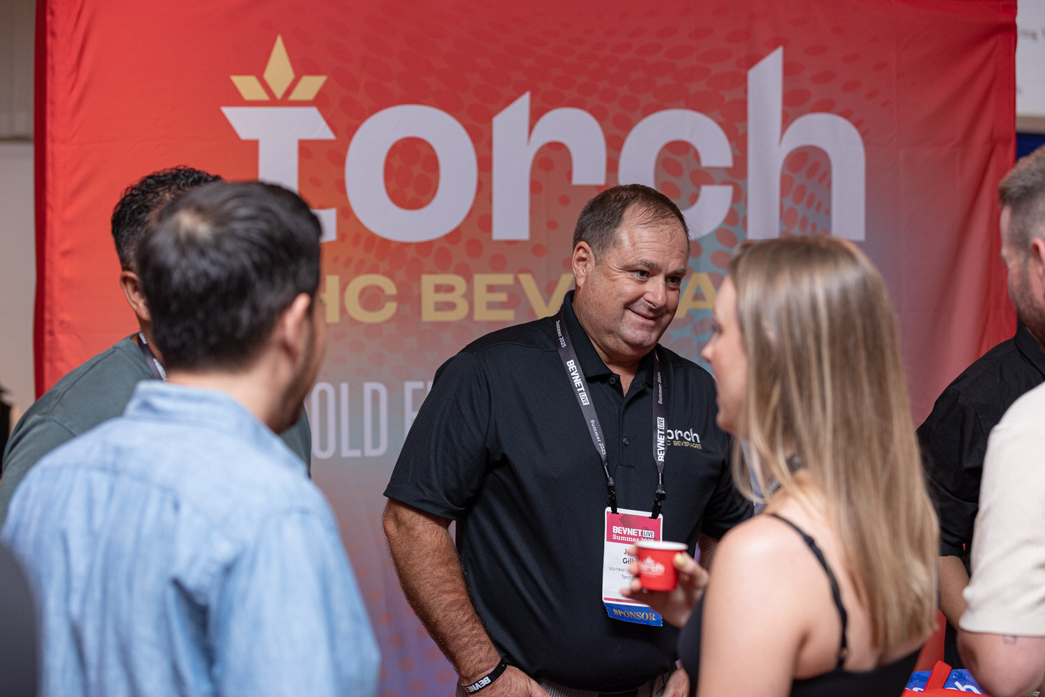 A man in a black polo smiles beside other attendees in front of a red Torch THC beverage backdrop.