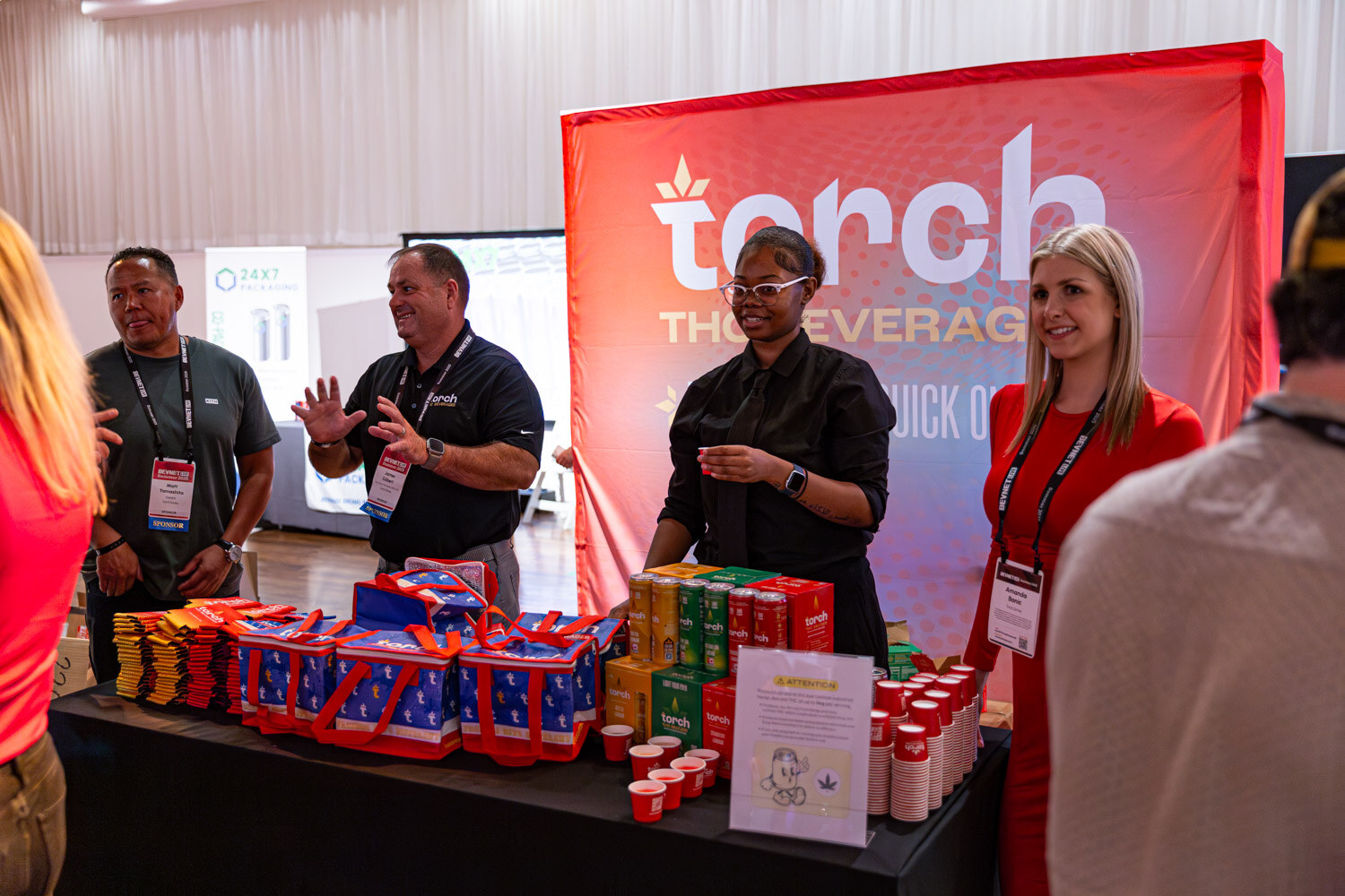 Four people stand behind a table with red bags in front of a Torch THC beverage backdrop.