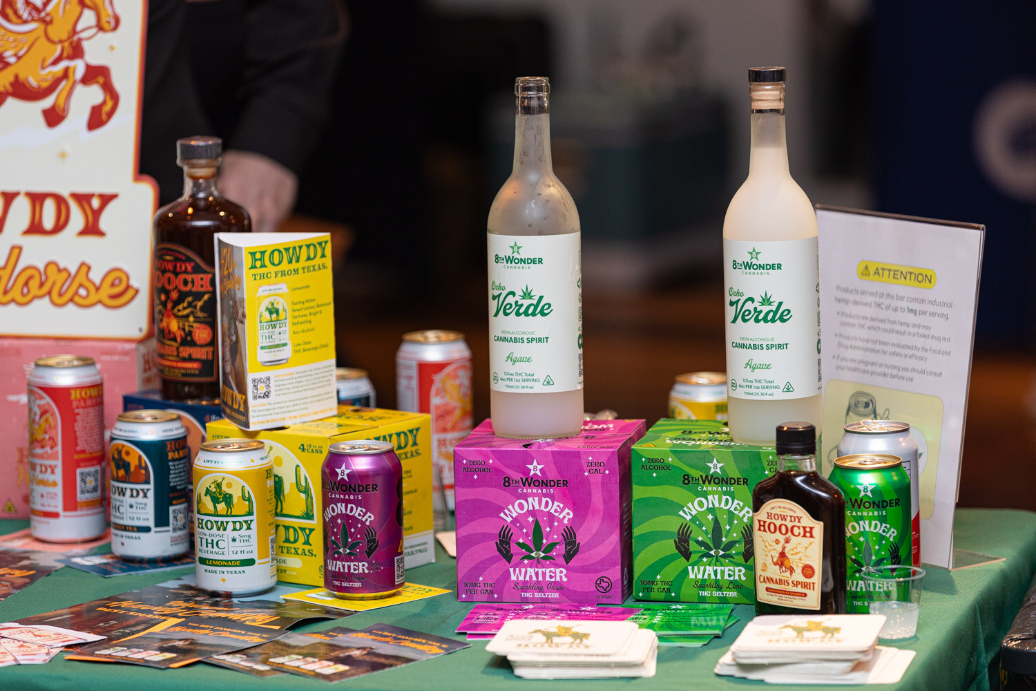 A table covered in Howdy cans and bottles and pink and green 8 Wonder cannabis products.