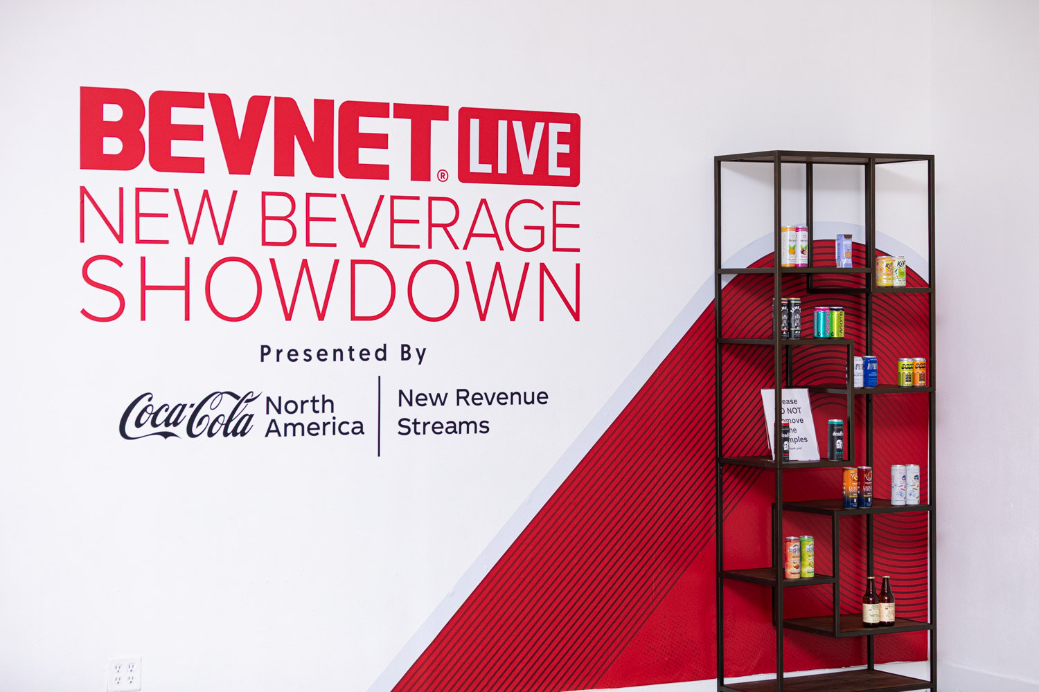 A BevNET Live New Beverage Showdown wall sign with a small shelf of drink cans.