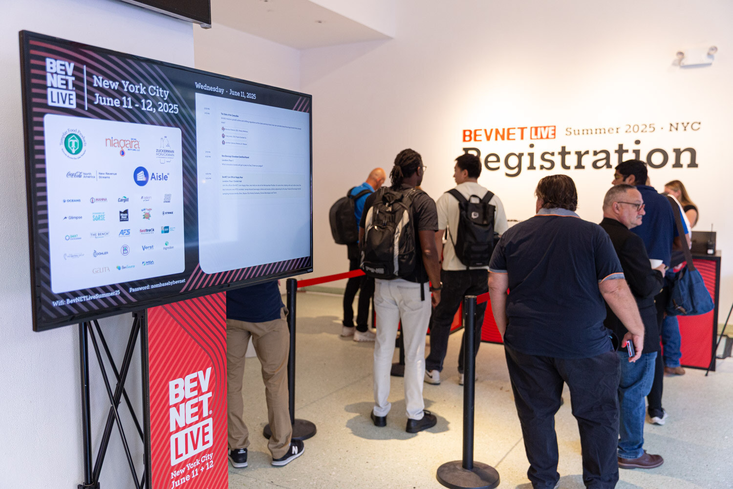 A line of attendees in front of a Registration wall sign and a tall screen showing the conference schedule.