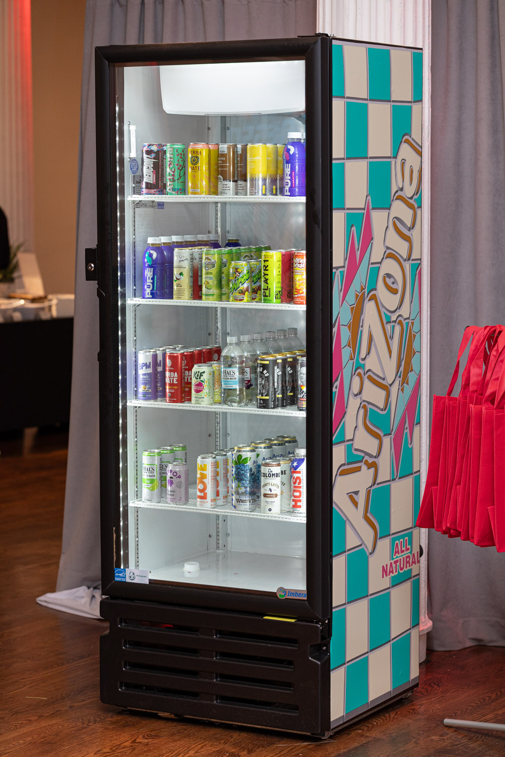 A tall glass-door refrigerator with an Arizona checker pattern and shelves of beverage cans.