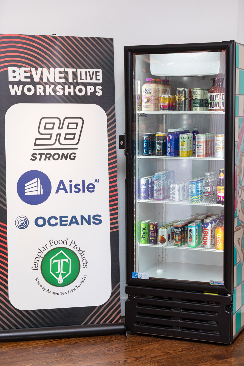 A refrigerator full of cans next to a BevNET Live Workshops sign listing 98 Strong, Aisle, Oceans and Templar.