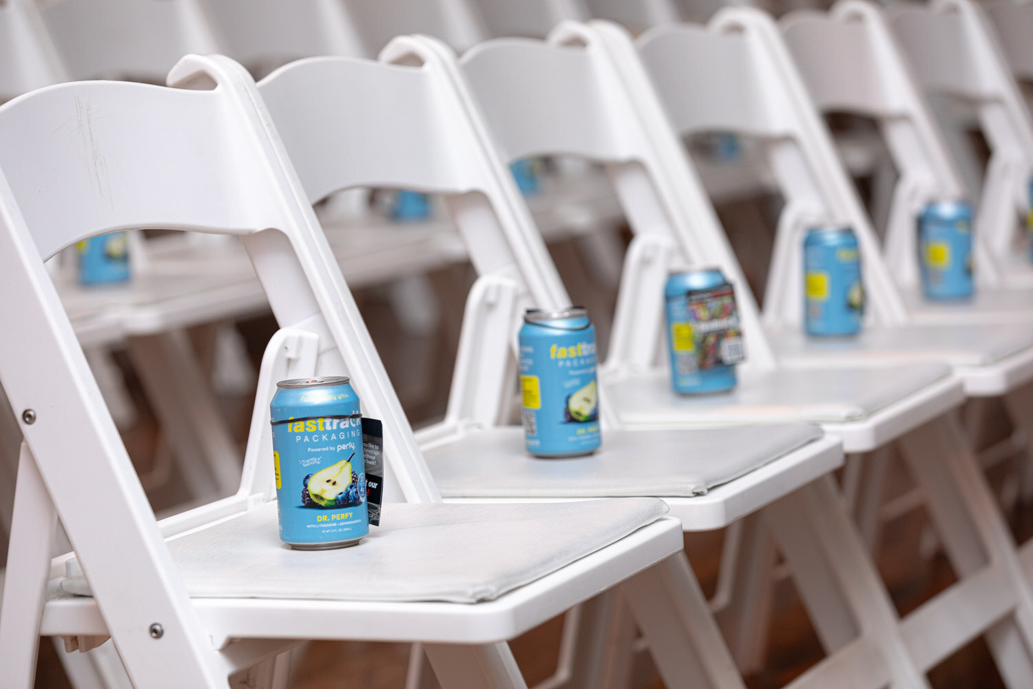 Blue beverage cans from Fasttrack Packaging sit on white folding chairs.