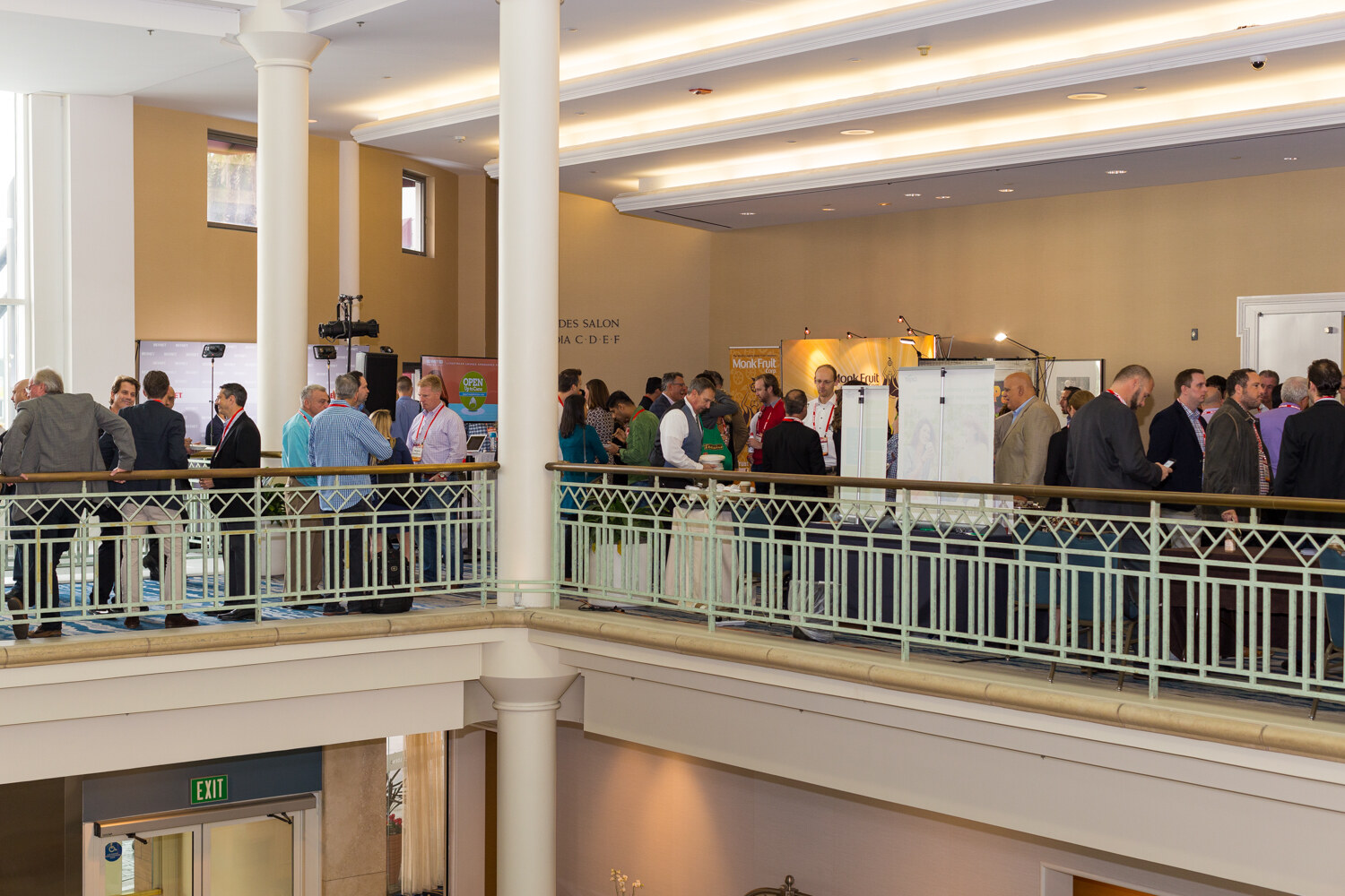 View from a mezzanine of attendees mingling at tables and booths on the floor below, with a Monk Fruit banner and an Open Up to Cans sign.