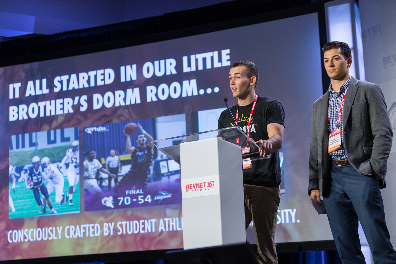 A man in a black Sunniva T-shirt speaks at the lectern beside a man in a gray blazer and checked shirt, in front of a screen with college sports photos and the line Consciously crafted by student athletes.