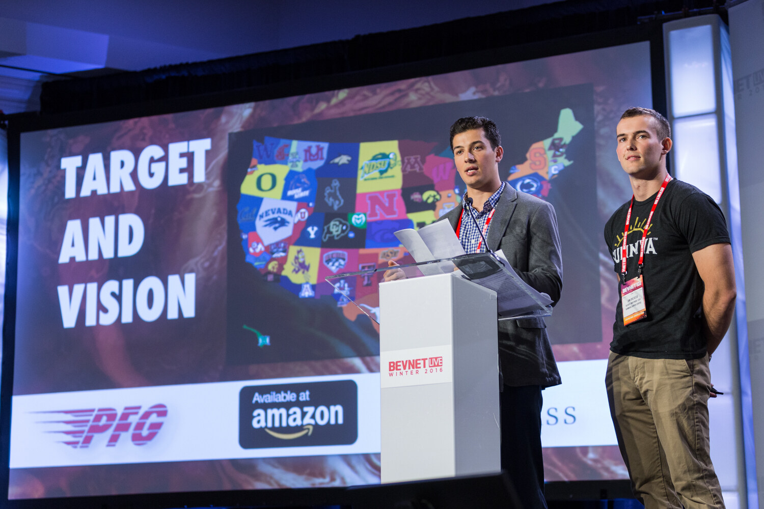 A young man in a gray blazer holds notes at the lectern while a man in a black Sunniva shirt stands beside him; the screen shows a map of college logos with PFG and Available at Amazon badges.