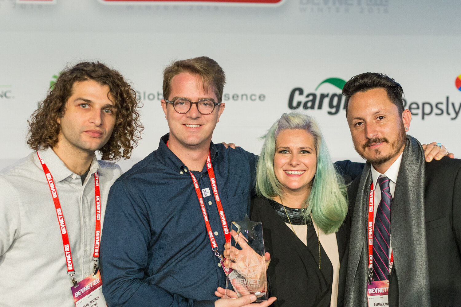 Four people with BevNET Live lanyards stand close together; the second from left holds a clear glass star-shaped trophy and the backdrop shows Cargill, Global Essence and Repsly logos.