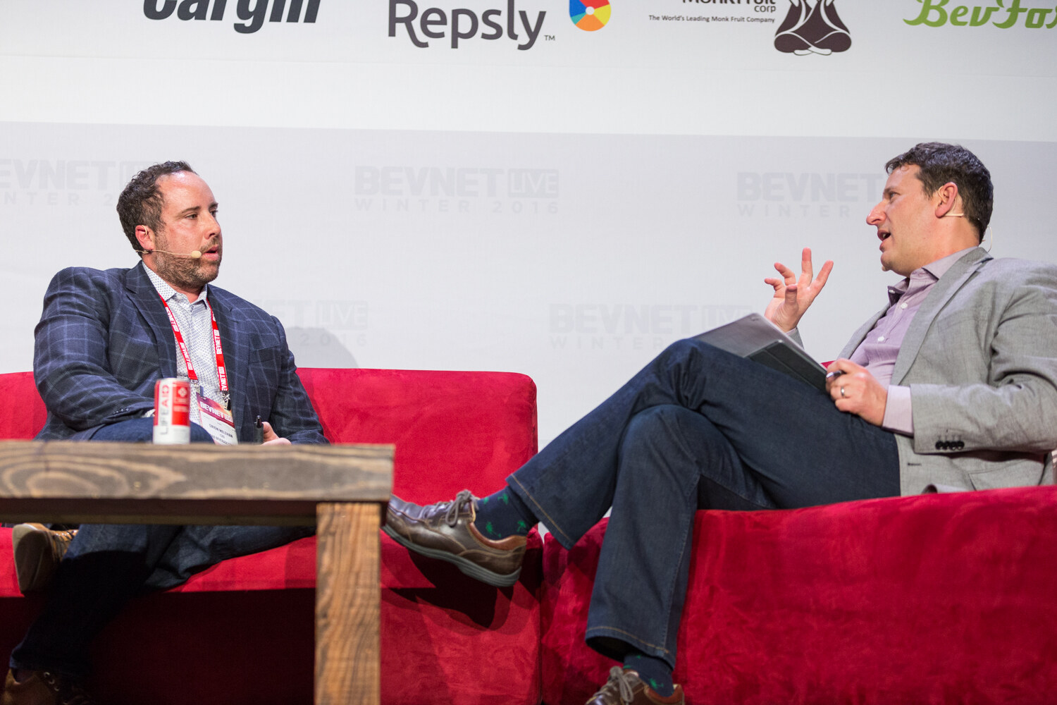 A bearded man in a navy plaid blazer and BevNET Live badge sits beside a red can on a wooden table, facing a moderator in a gray blazer who gestures, with Cargill, Repsly and Monk Fruit logos above.