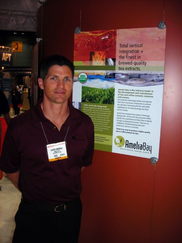 Jason Crandall of Amelia Bay, in a dark maroon polo and badge, stands beside an Amelia Bay poster about brewed-quality tea extracts at IFT 2007.