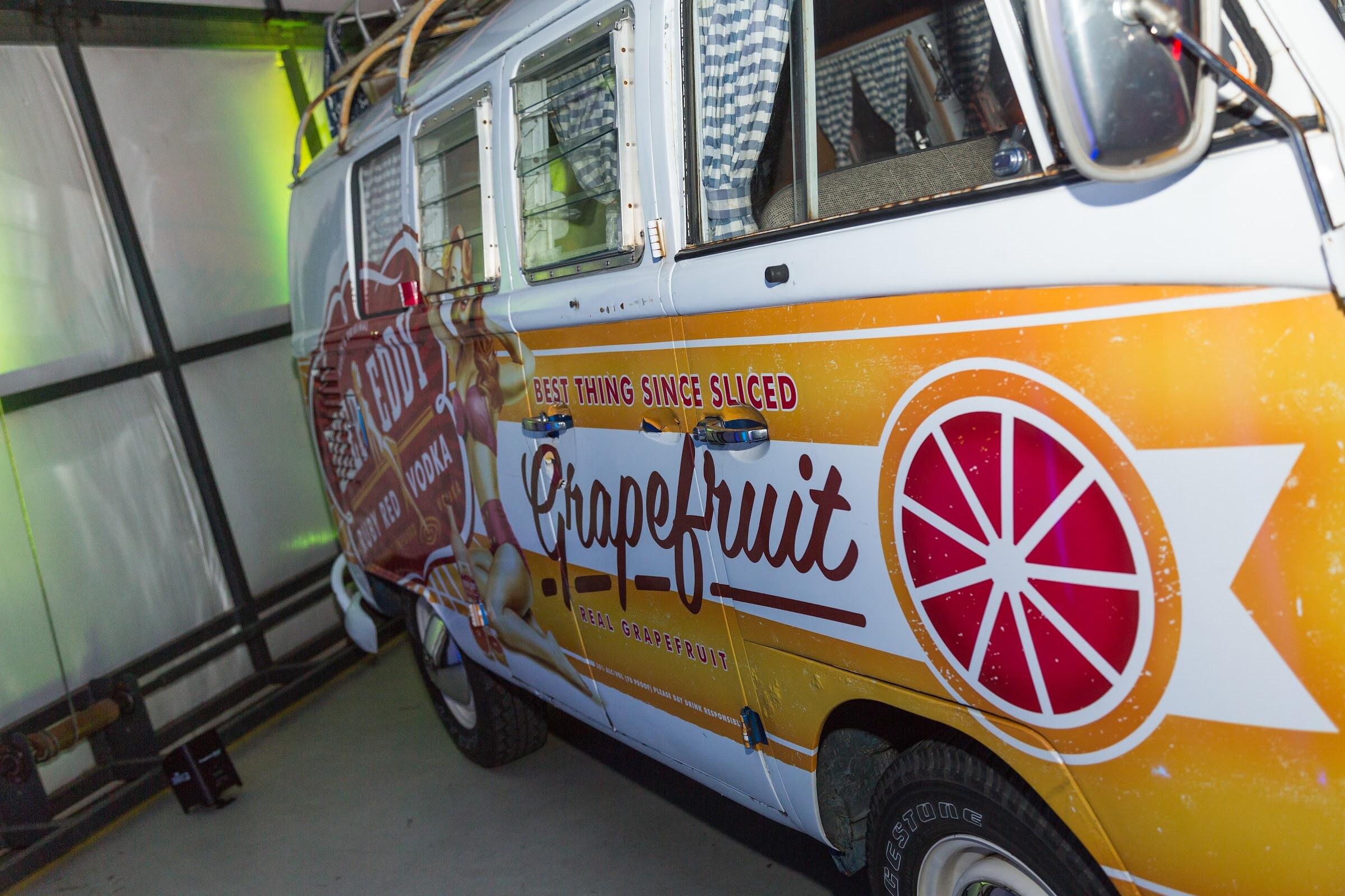 Side view of a vintage VW camper van painted orange and white with Deep Eddy Ruby Red Vodka graphics and a large Grapefruit slogan that reads Best thing since sliced.