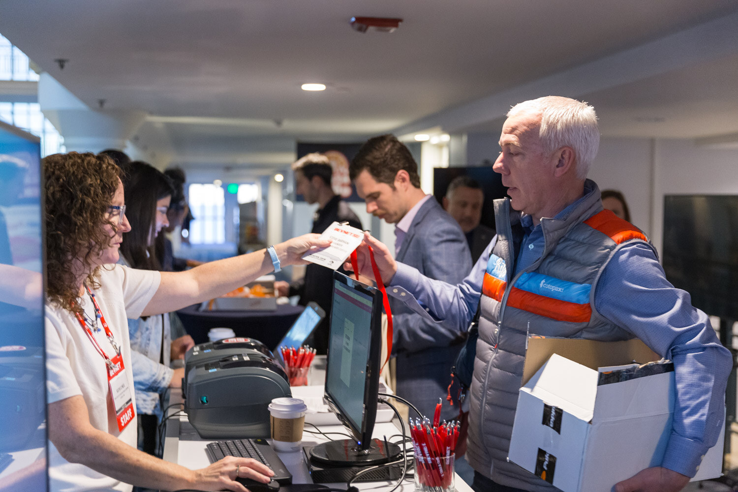 Woman behind a registration desk handing a lanyard to a man with a box.