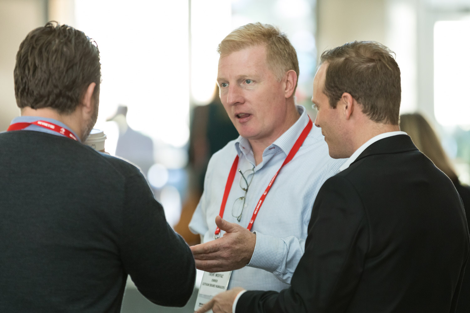 Two men in lanyards talking close together in a bright room.