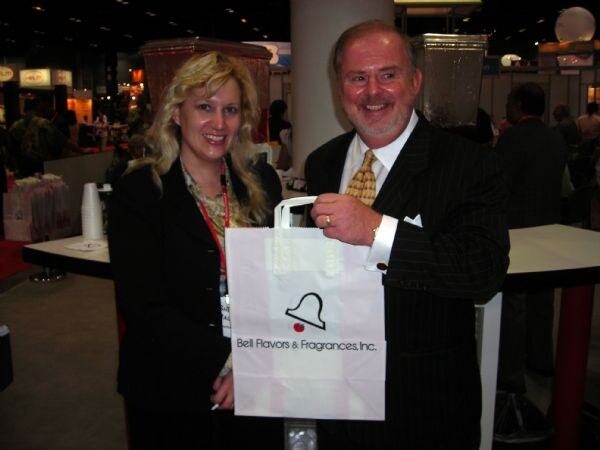 Sheila and Jeff of Bell Flavors & Fragrances smile as the man holds a white Bell Flavors & Fragrances, Inc. paper bag on the IFT 2007 show floor.