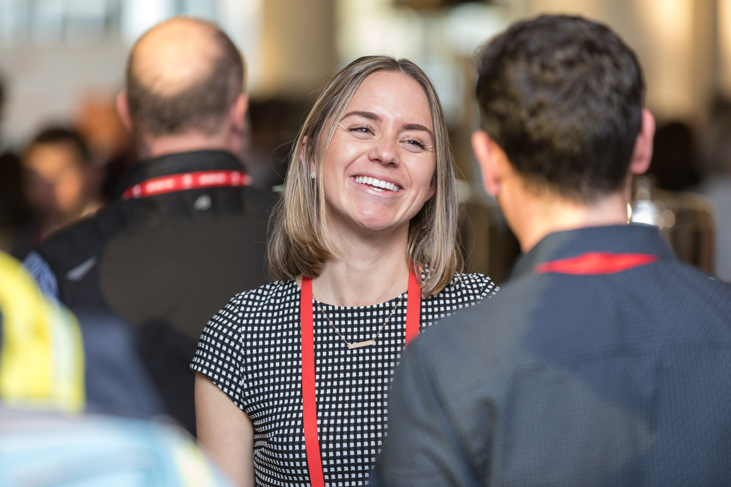 Woman with a red lanyard smiling at the camera in a crowded room.