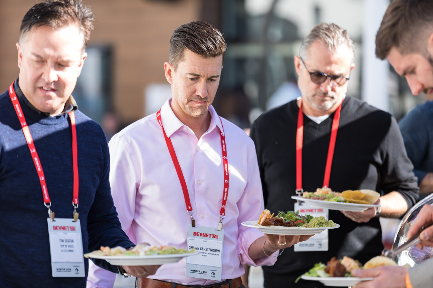 Three men in lanyards holding plates at a lunch buffet.