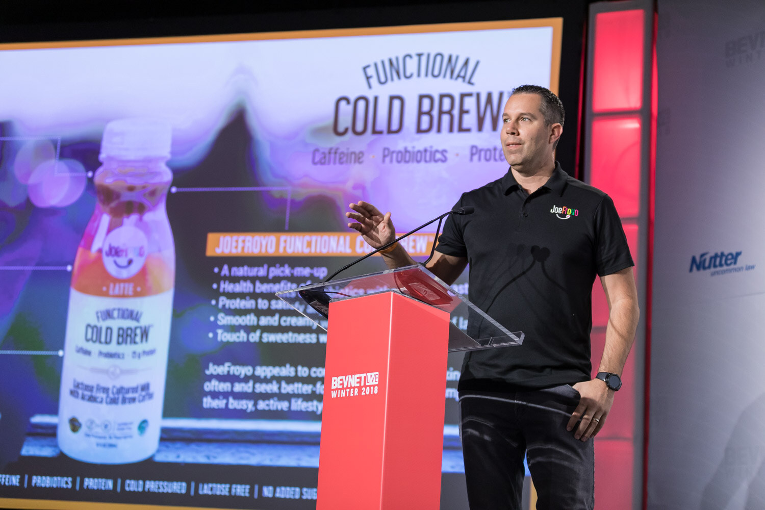 Man in a black polo gesturing at a podium next to a Functional Cold Brew slide.