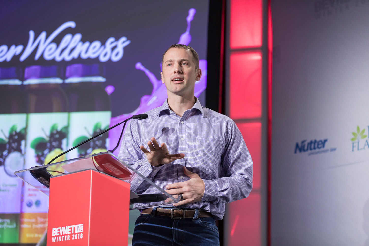 Man in a light purple shirt at a podium next to a purple slide titled Discover Wellness.