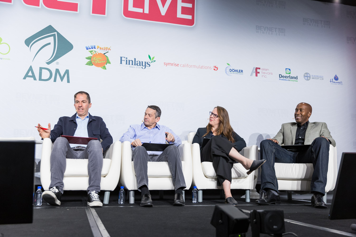 Four people seated in white armchairs on a stage in front of a BevNET Live backdrop.