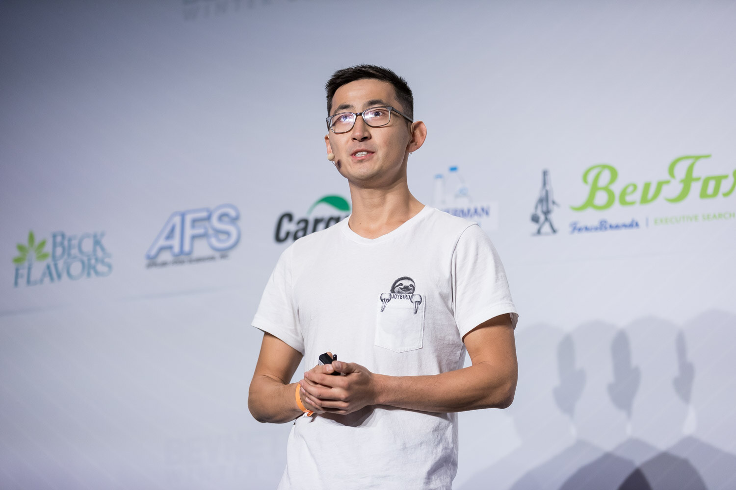 Man in glasses and a white t-shirt holding a clicker on stage.