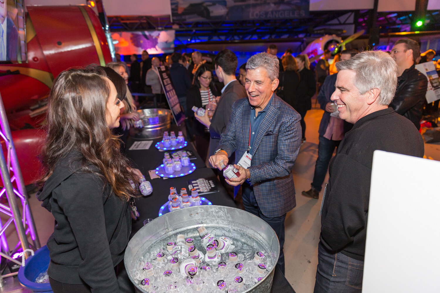 Woman and two men laughing around a tub of small drink bottles on ice.