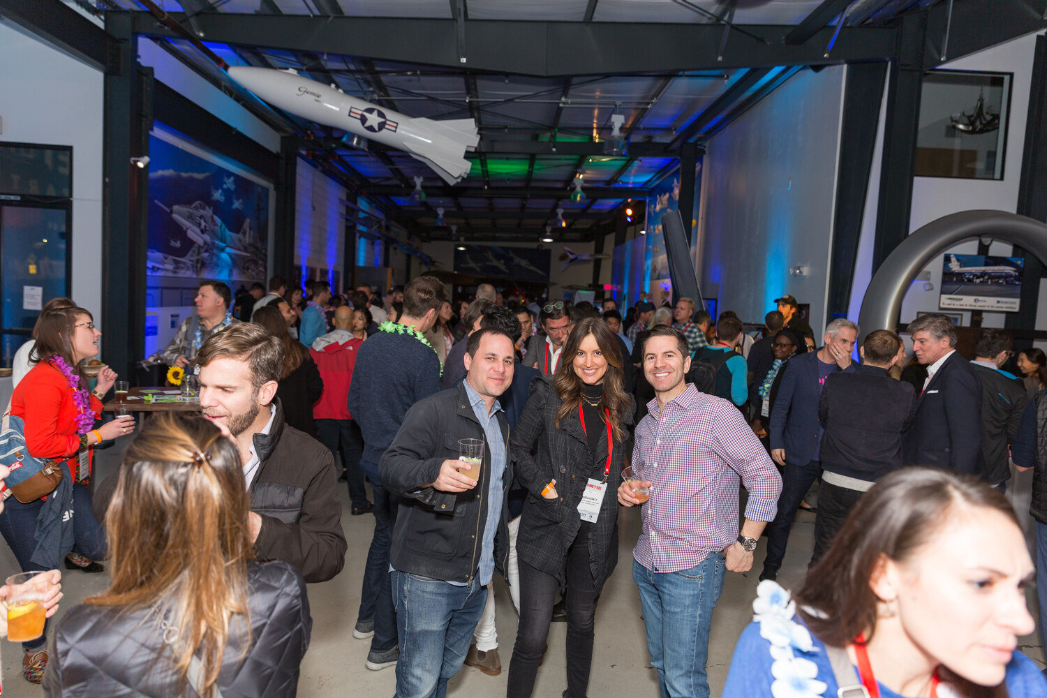 Crowd of smiling guests in a hangar with a plane suspended overhead.