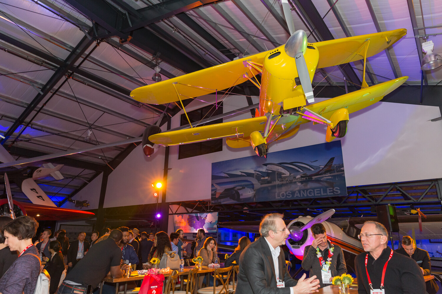 Wide view of guests at wooden tables under a yellow biplane.