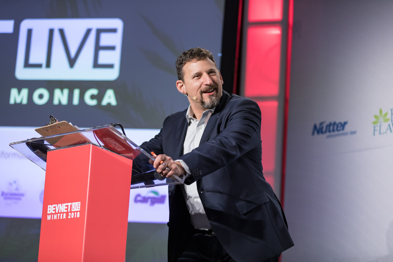 Man at a red podium gesturing beside a large screen reading BevNET Live Winter 2018 Santa Monica.