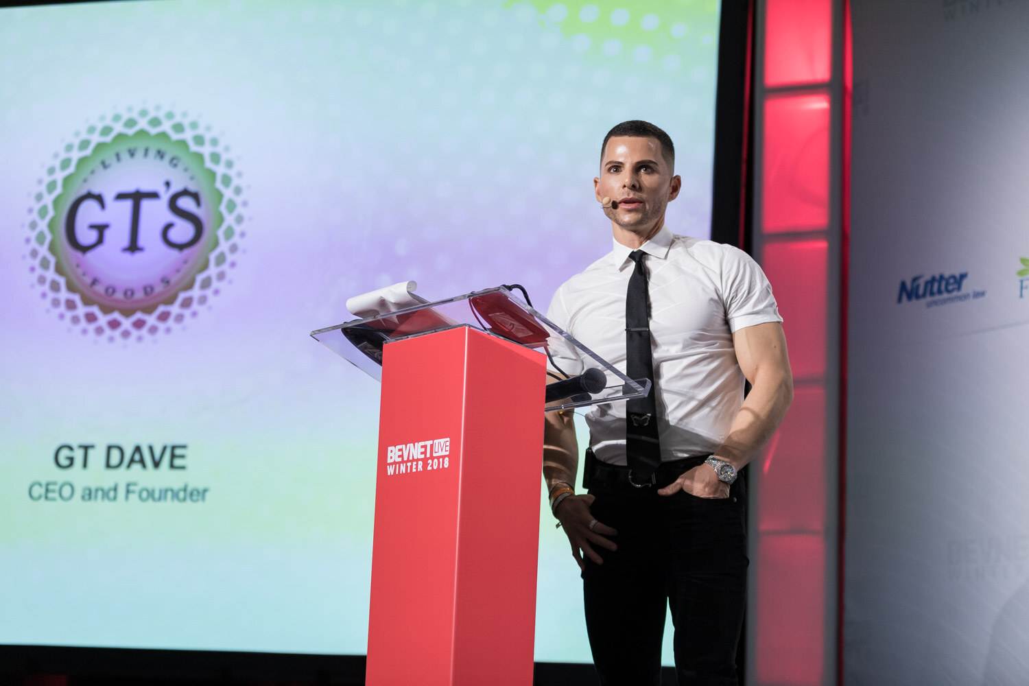 Man in a white shirt and tie beside a podium and a slide with a GT's logo.
