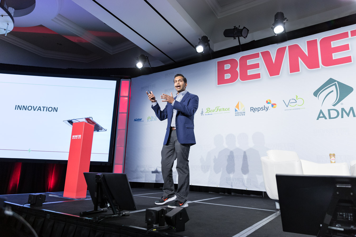 Man in a blazer on a large stage beside a screen reading Innovation.