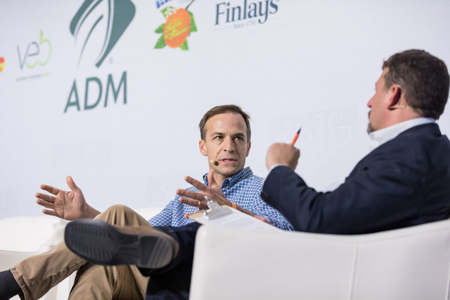 Man in a blue shirt gesturing while talking to a seated interviewer on stage.
