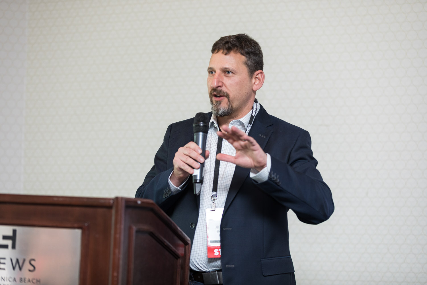 Man in a navy blazer speaking at a wooden lectern marked Loews.