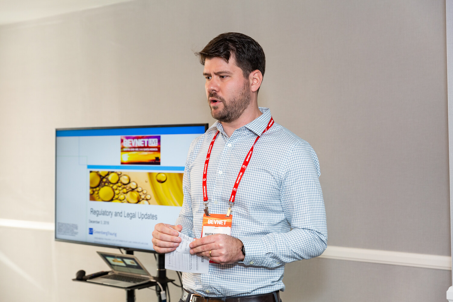 Man in a light blue shirt with an orange badge holding a clicker beside a screen titled Regulatory and Legal Update.