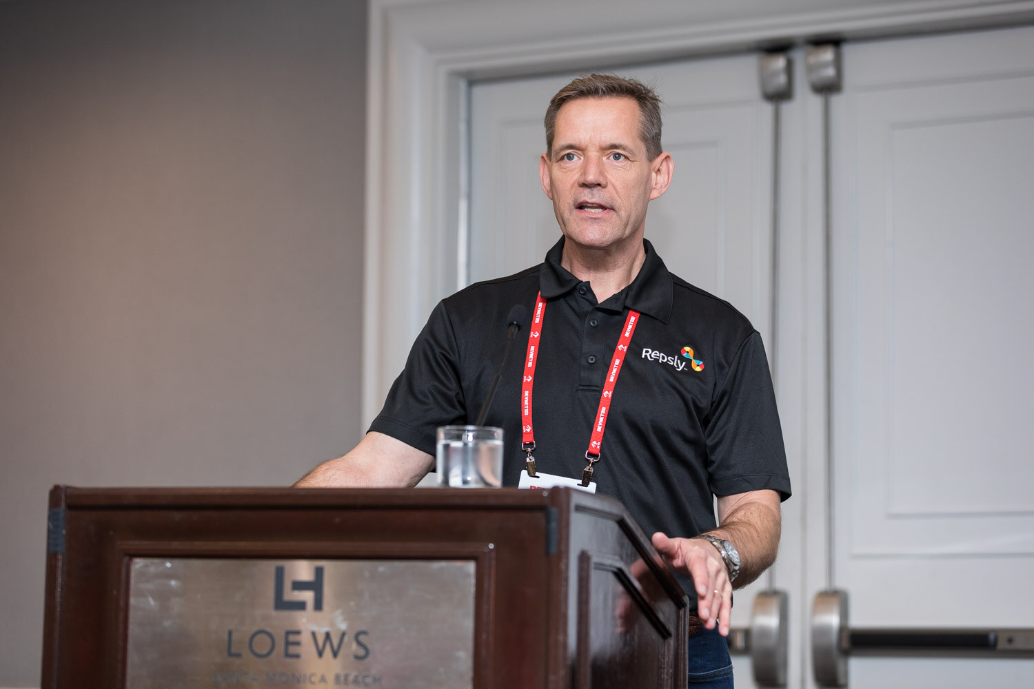 Man in a black Repsly polo with a lanyard speaking at a wooden lectern.