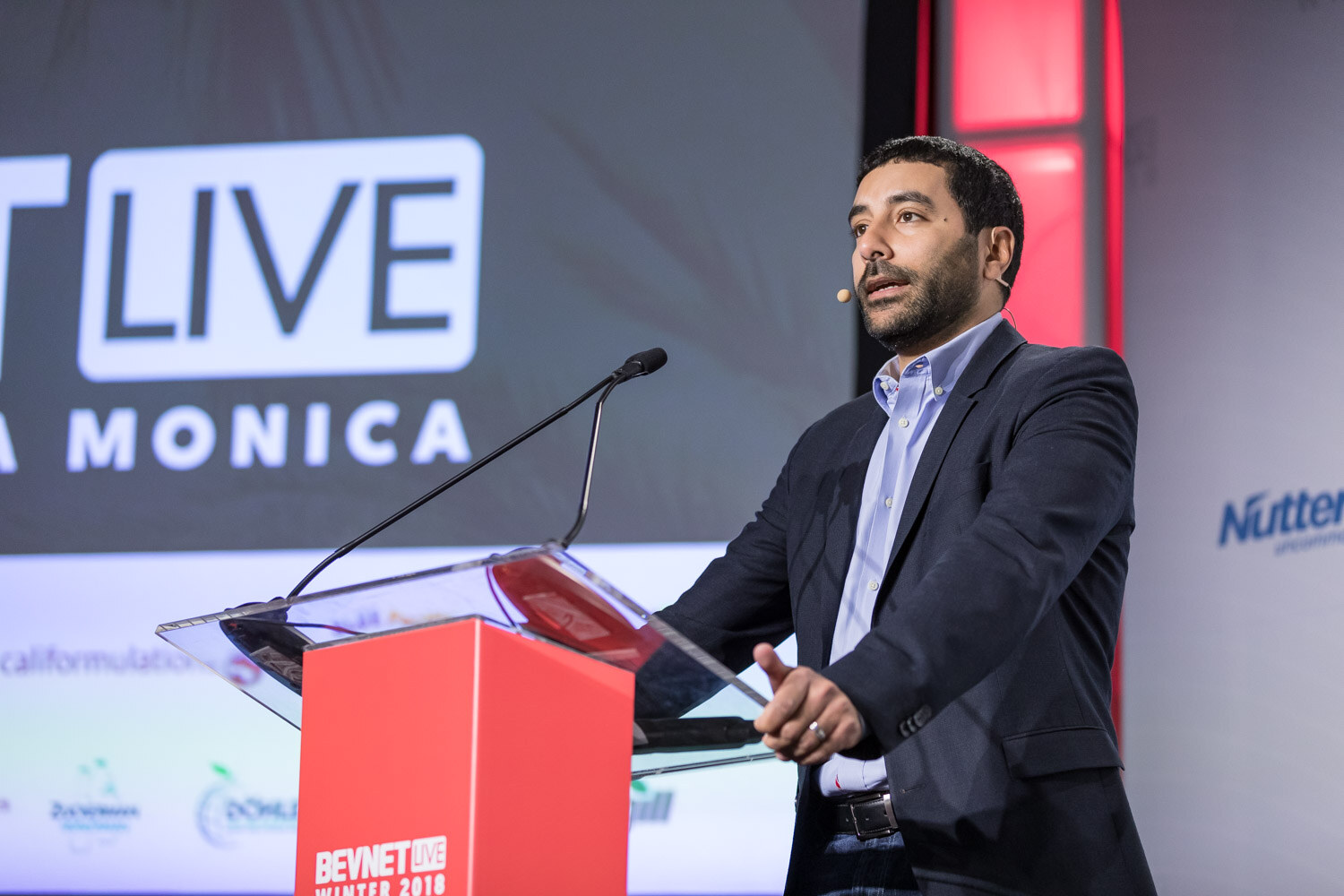 Man at a podium on stage in front of a Santa Monica event graphic.
