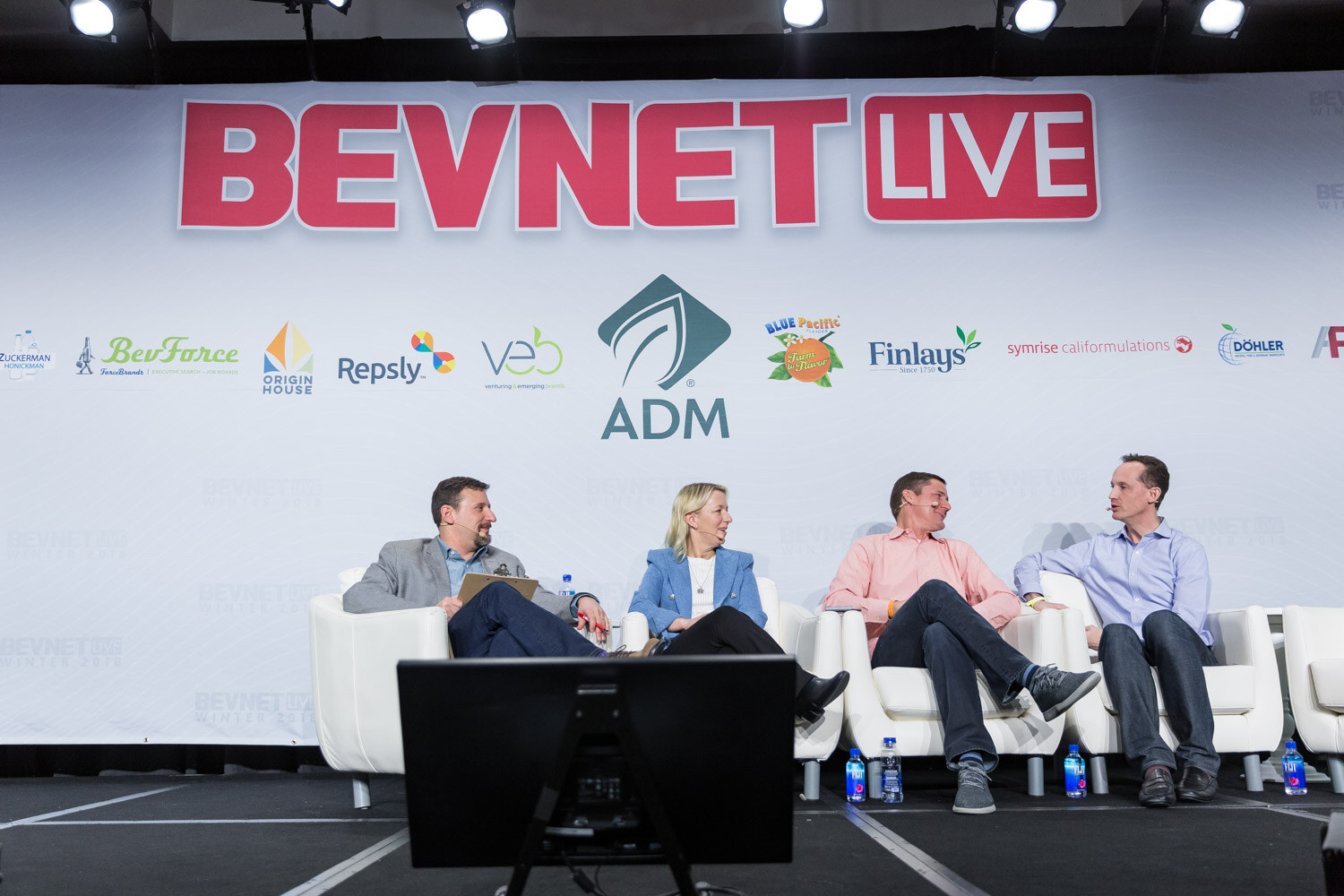 Four people in white armchairs on stage under a BevNET Live sign.